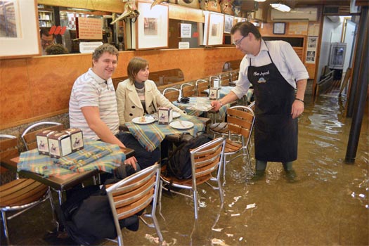 A waiter serves coffee to tourists in his flooded bar in Venice